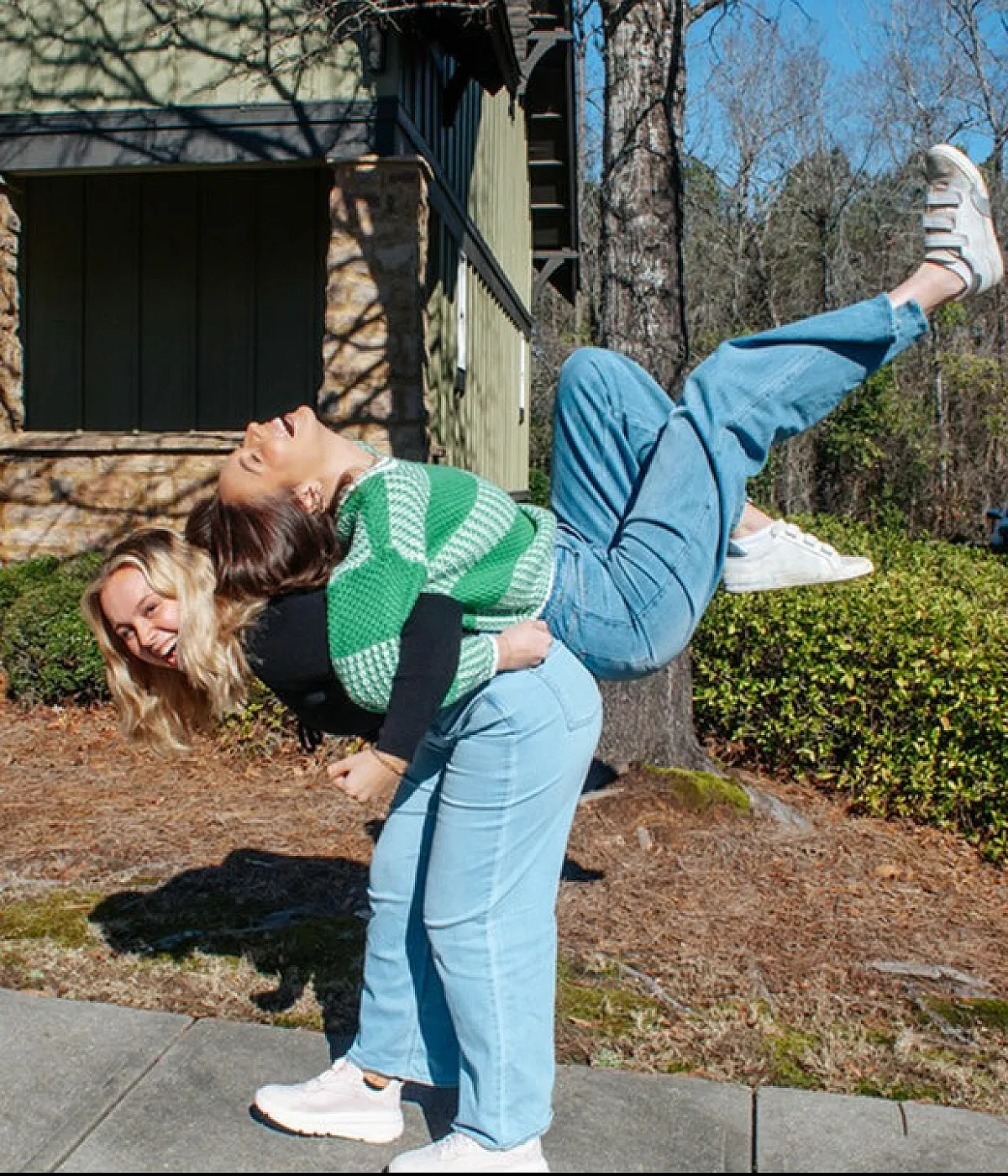 Joyful duo having fun outdoors in front of charming cottage-style apartments, showcasing vibrant community living.