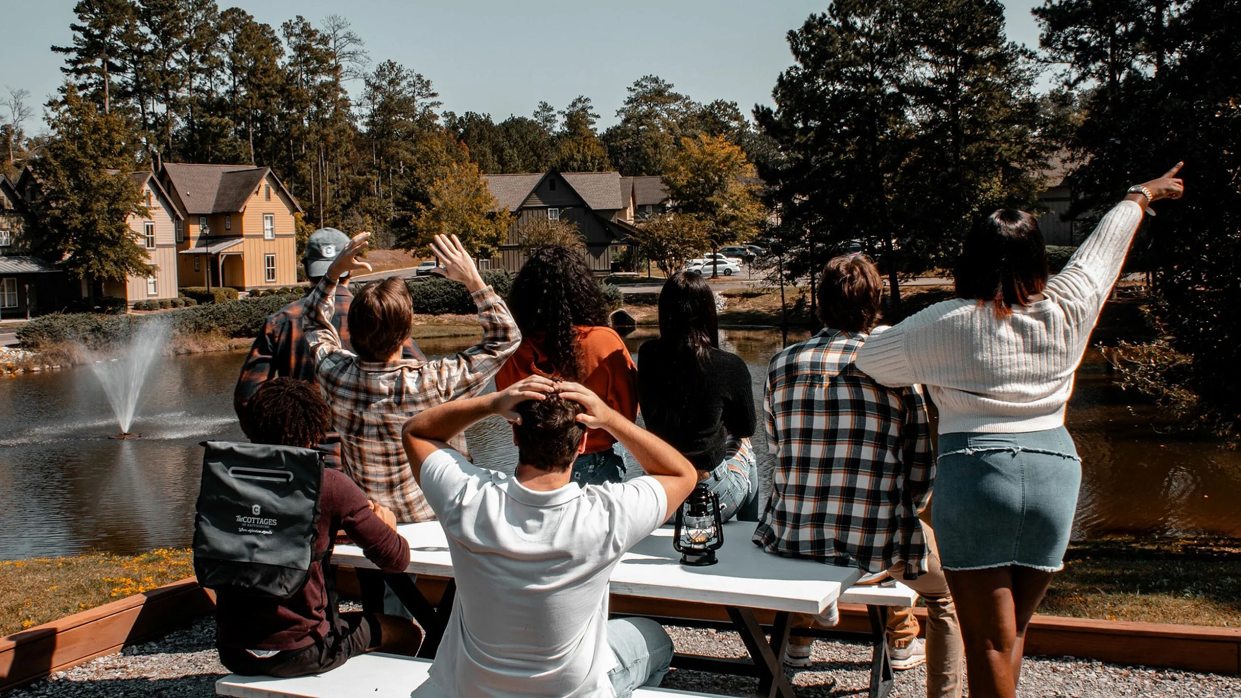 Vibrant lakeside view with a group of people enjoying a sunny day near charming houses and a serene fountain.