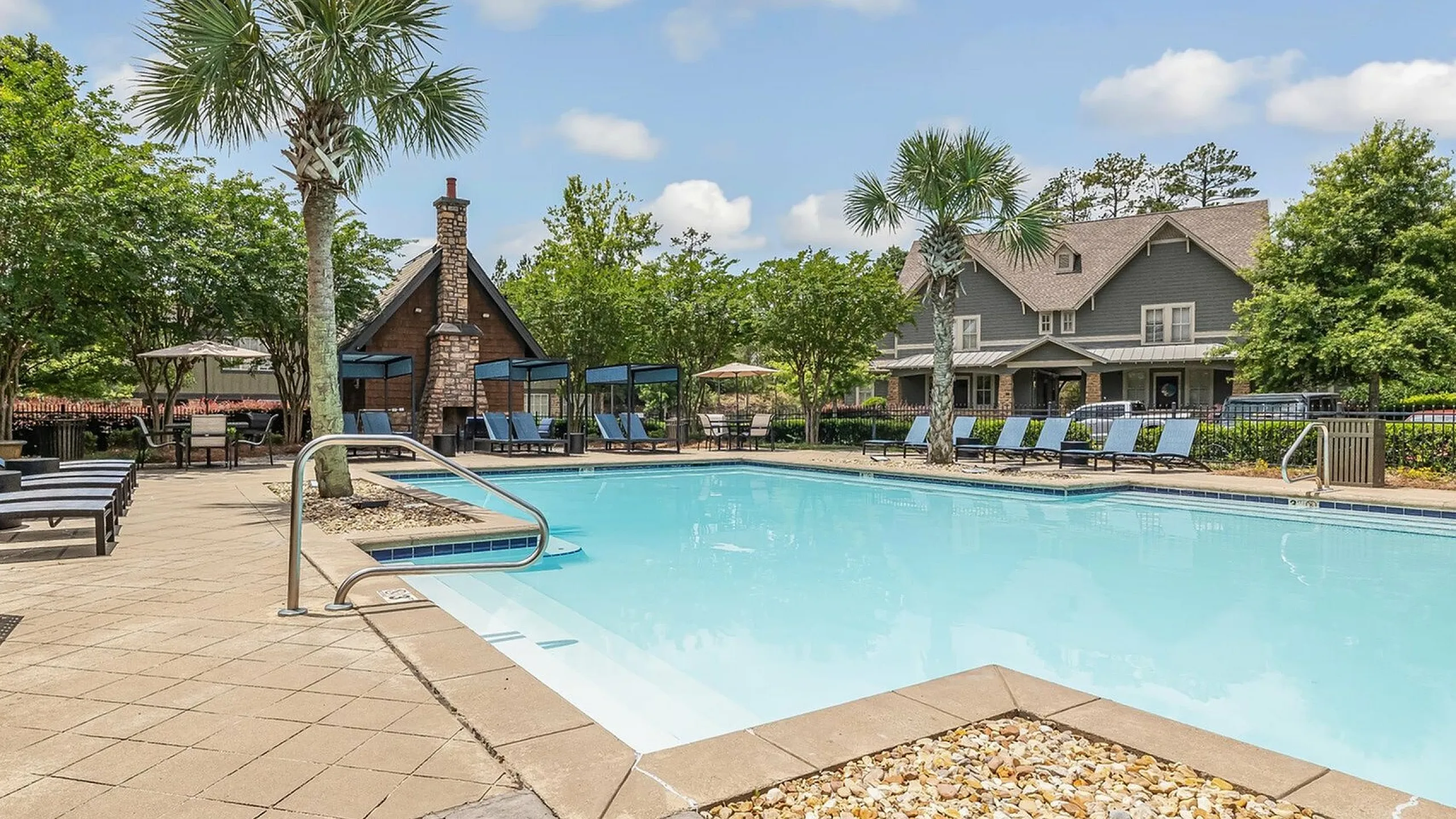 Inviting apartment complex pool area with lush greenery and cozy lounge chairs, perfect for relaxation and leisure.
