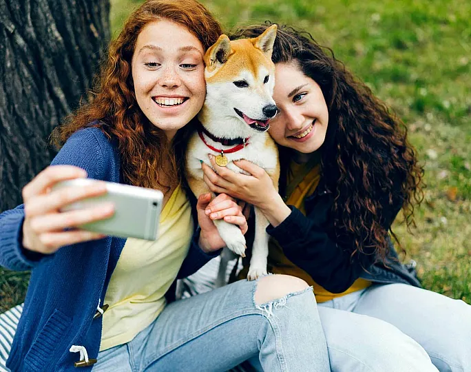 Joyful selfie moment with two friends and a Shiba Inu dog in a lush green park setting.