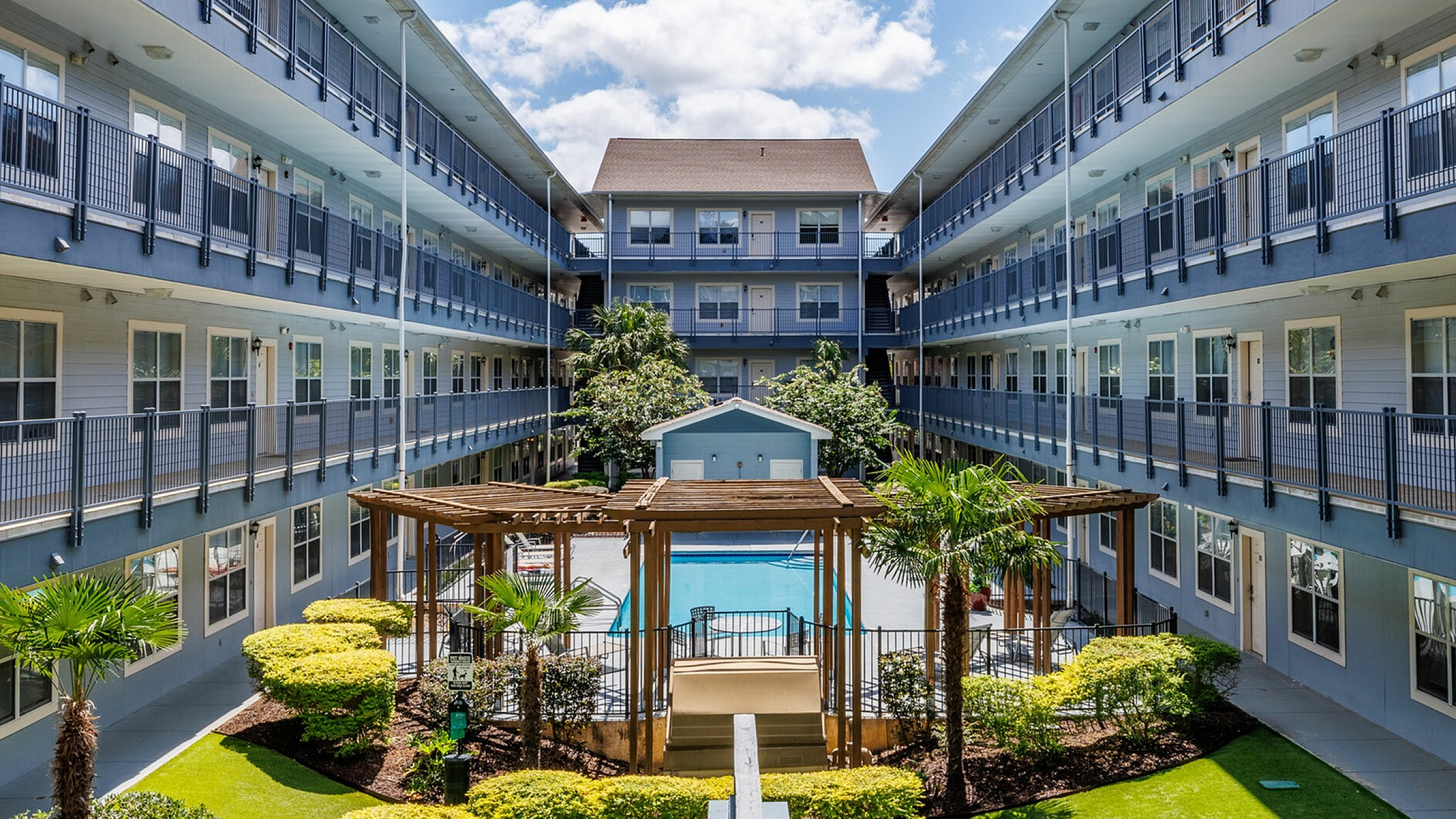 Beautifully designed apartment complex courtyard with lush landscaping, a central swimming pool, and modern architecture.