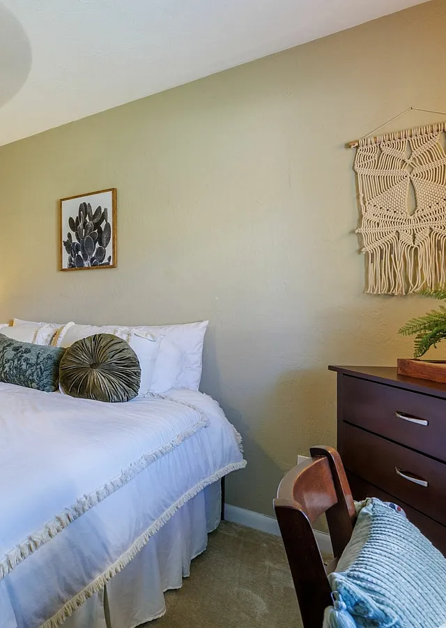 Inviting bedroom with a cozy atmosphere, featuring a plush bed with stylish cushions, warm lighting, and elegant wall decor.