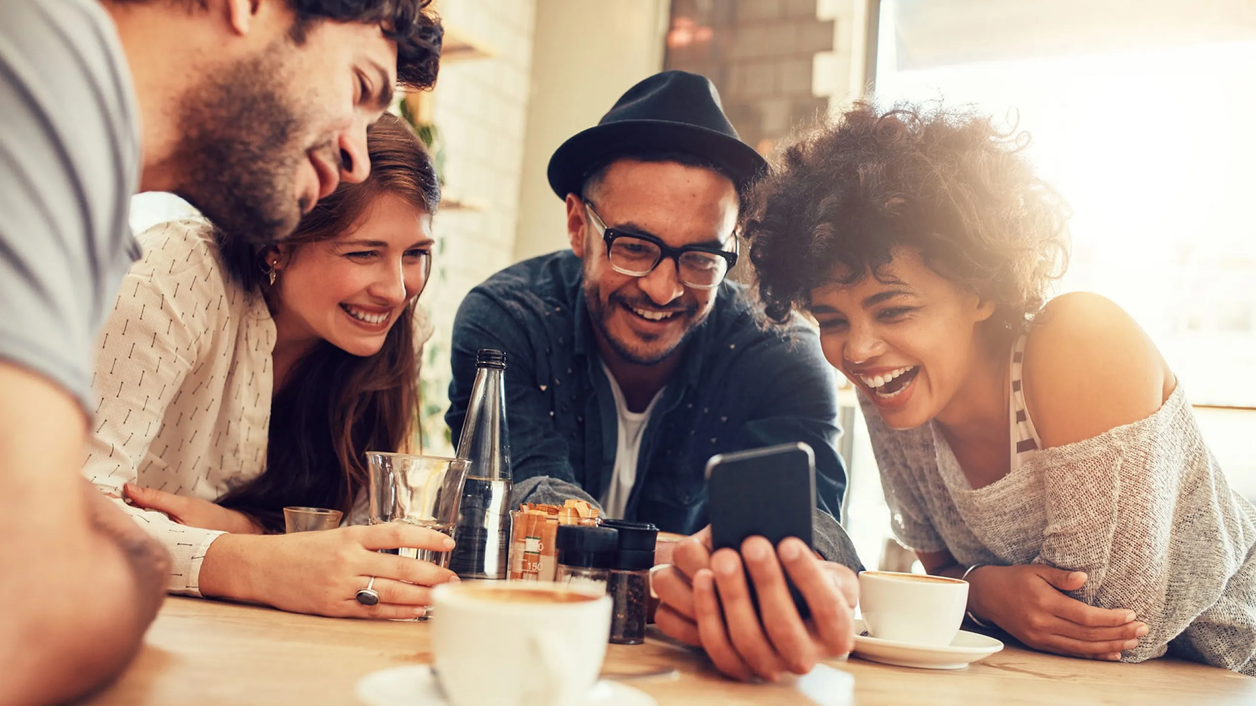 Joyful group of friends enjoying a lively conversation over coffee at a bright, modern cafe.