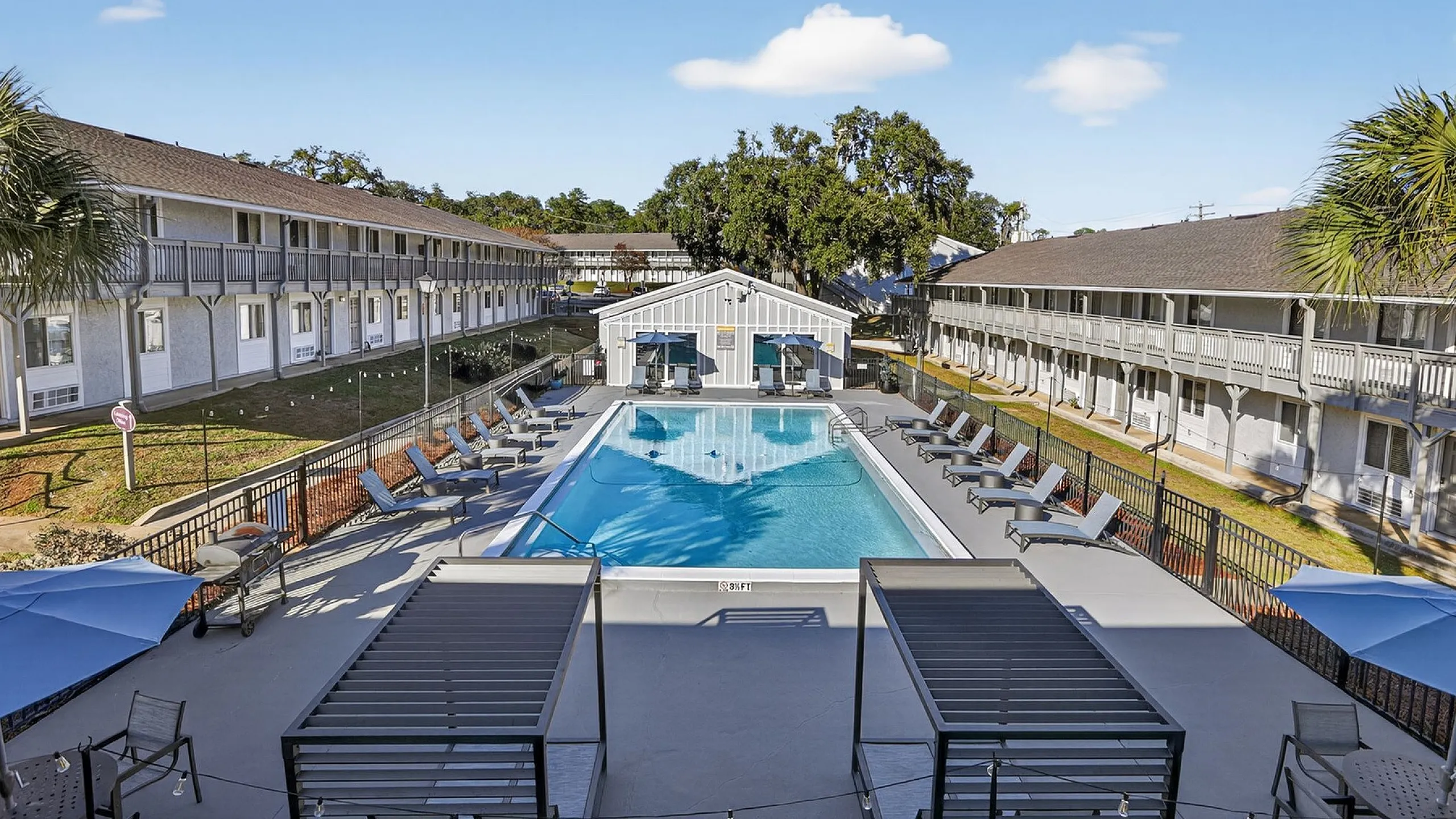 Inviting apartment complex with a central pool surrounded by stylish lounge chairs and lush greenery, perfect for relaxation and social gatherings.