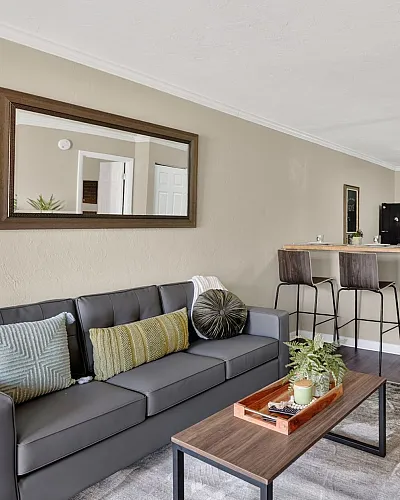 Modern open-concept living room with elegant gray sofa and stylish kitchen in the background, featuring warm neutral tones and chic decor.