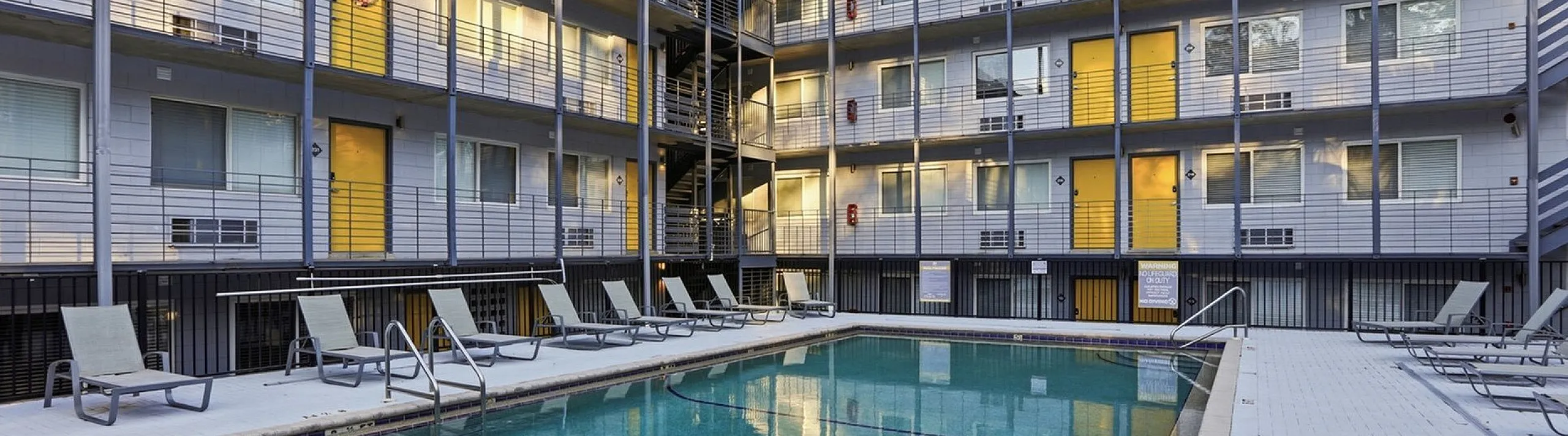 Modern apartment complex with a welcoming courtyard pool, cozy lounge chairs, and eye-catching yellow doors, perfect for relaxation and leisure.