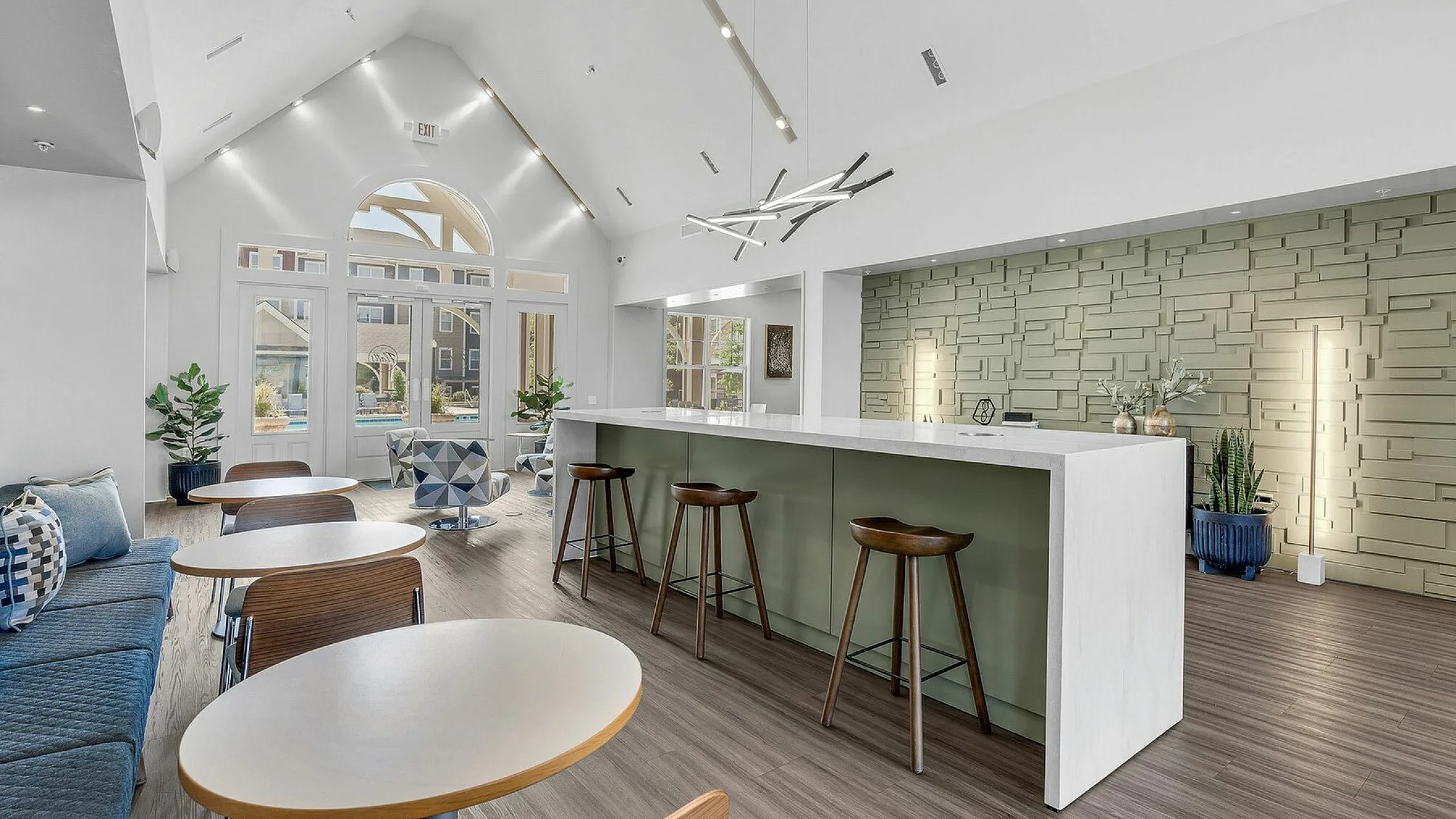 Modern communal space with sleek high ceilings, stylish bar seating, geometric accent wall, and abundant natural light for a welcoming atmosphere.