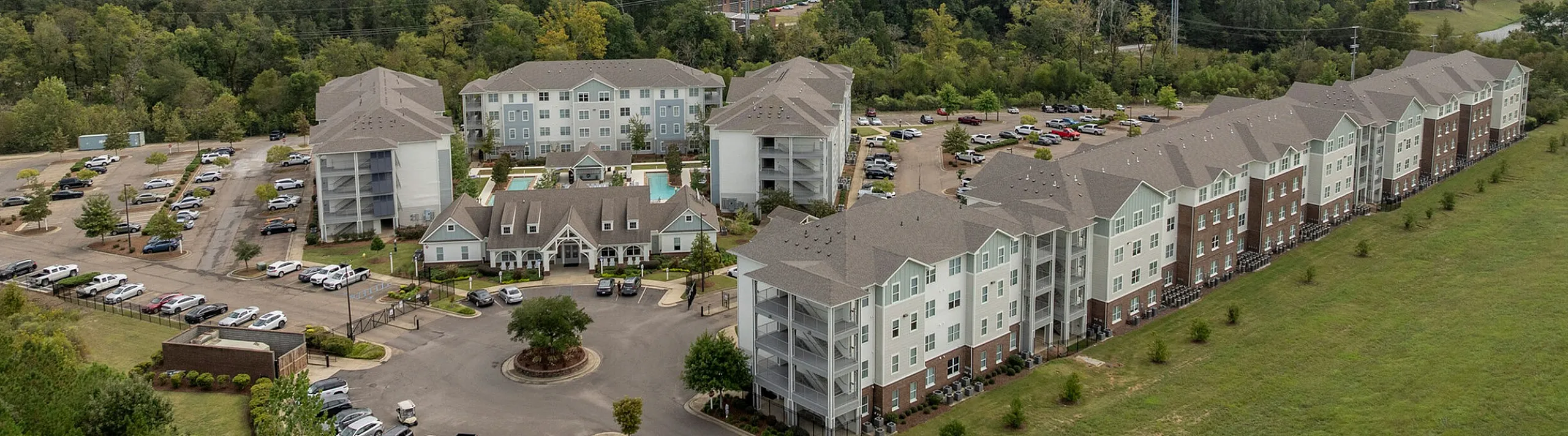Aerial view of a charming residential complex surrounded by lush greenery, featuring stylish multi-story buildings and ample parking space.