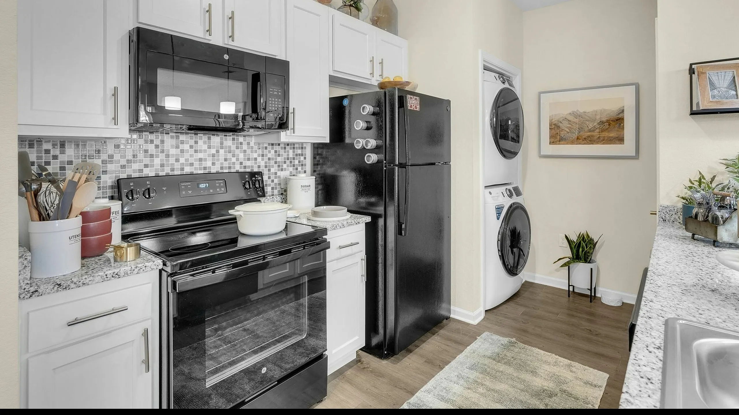 Contemporary kitchen with sleek black appliances, elegant granite countertops, and convenient in-unit laundry. Perfect for modern living.