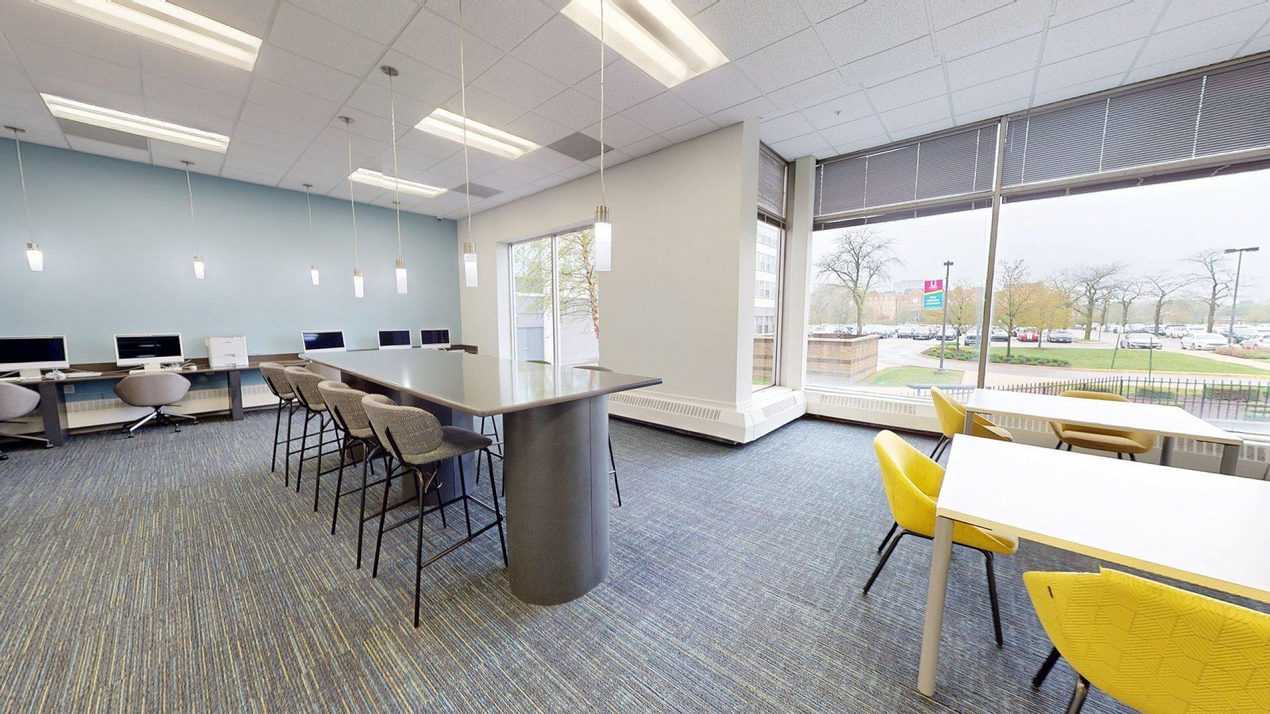 Modern and spacious co-working space with sleek desks, comfortable chairs, and large windows providing ample natural light and a view of the outdoors.