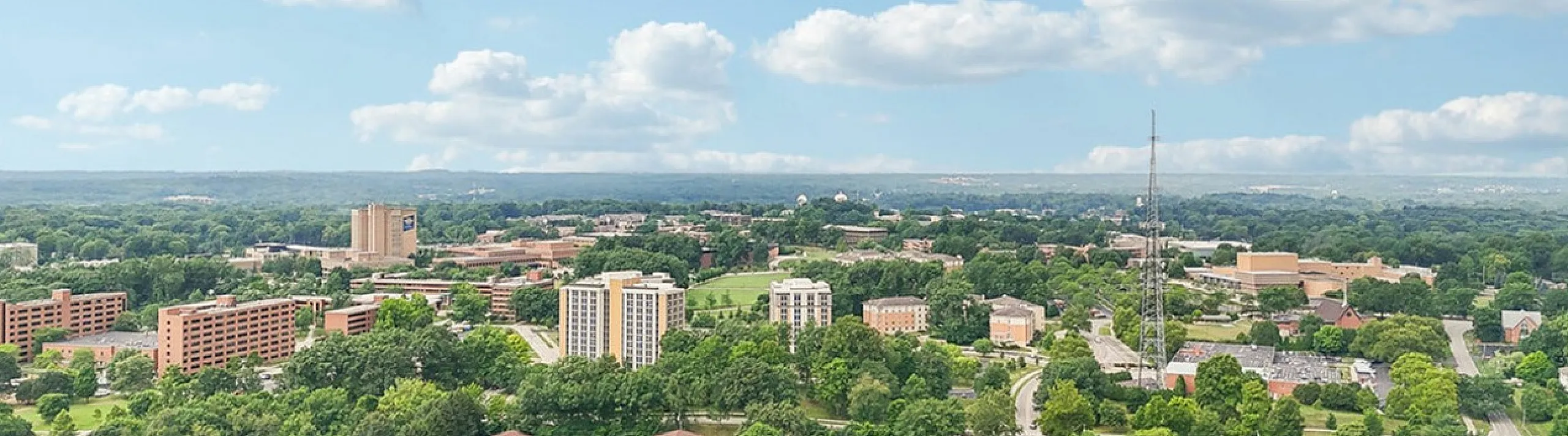 Aerial view showcasing a vibrant community with green spaces, modern apartment buildings, and a clear blue sky, highlighting a serene yet connected living environment.