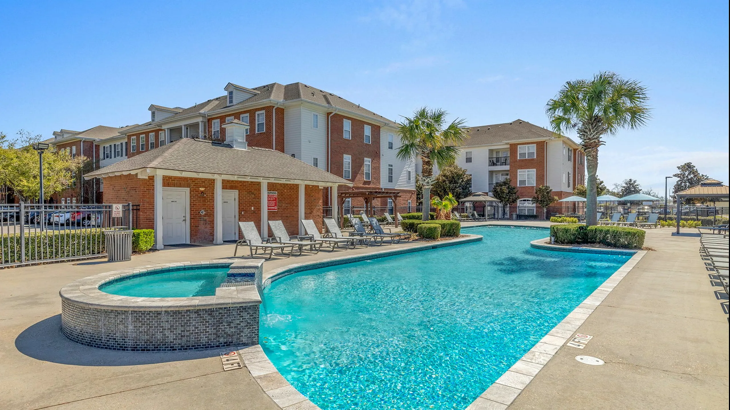 Luxurious apartment complex featuring a sparkling blue swimming pool with sun loungers, surrounded by elegant landscaping and modern architecture.
