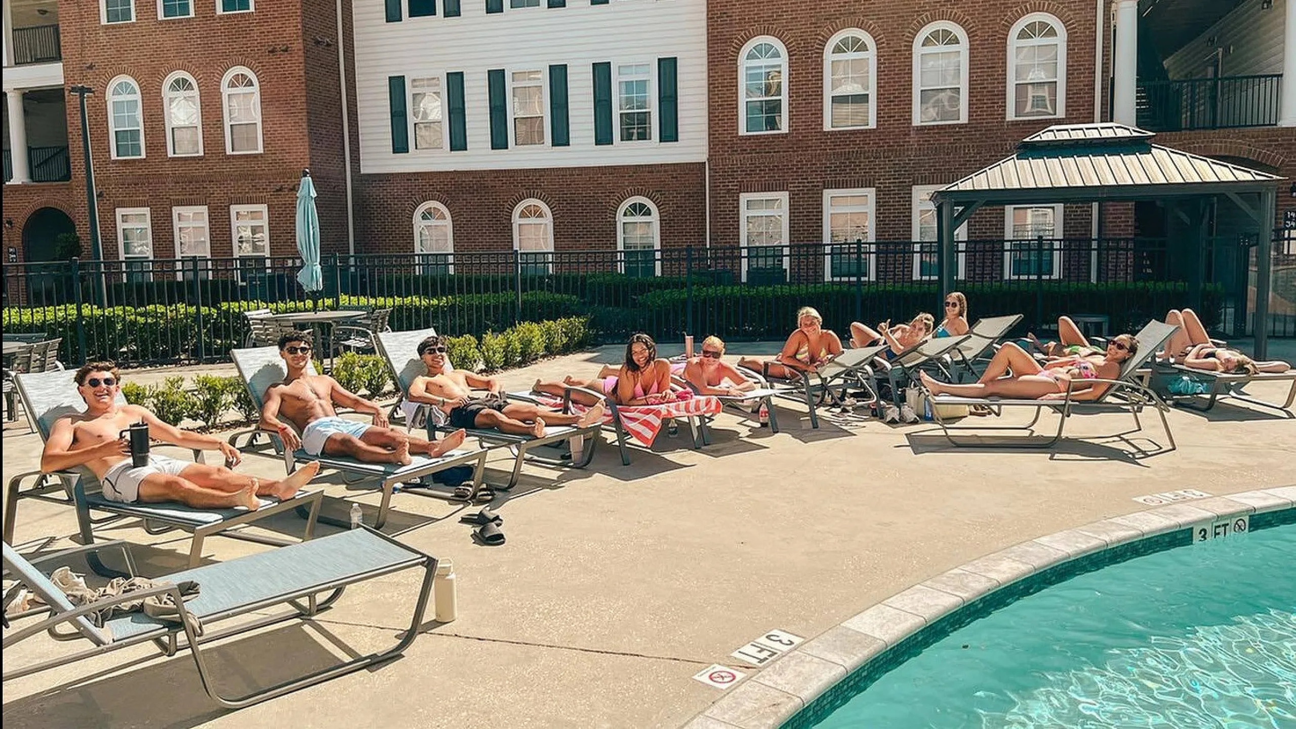 Vibrant apartment community with residents enjoying a sunny day by the pool, surrounded by elegant brick architecture.