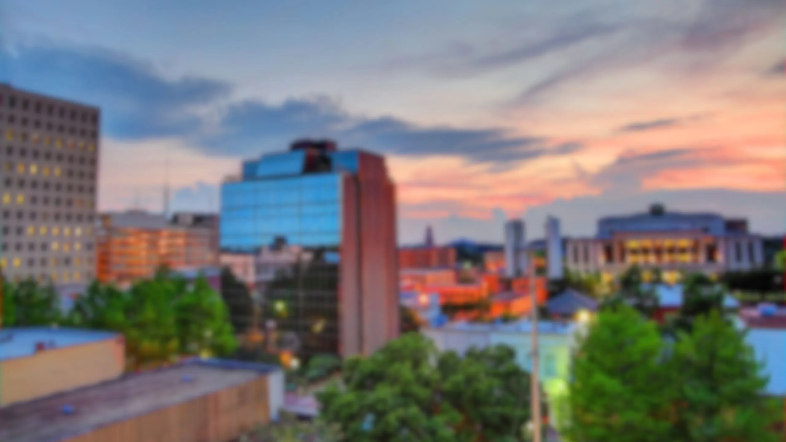 Vibrant cityscape at sunset featuring modern glass and brick buildings surrounded by lush greenery.