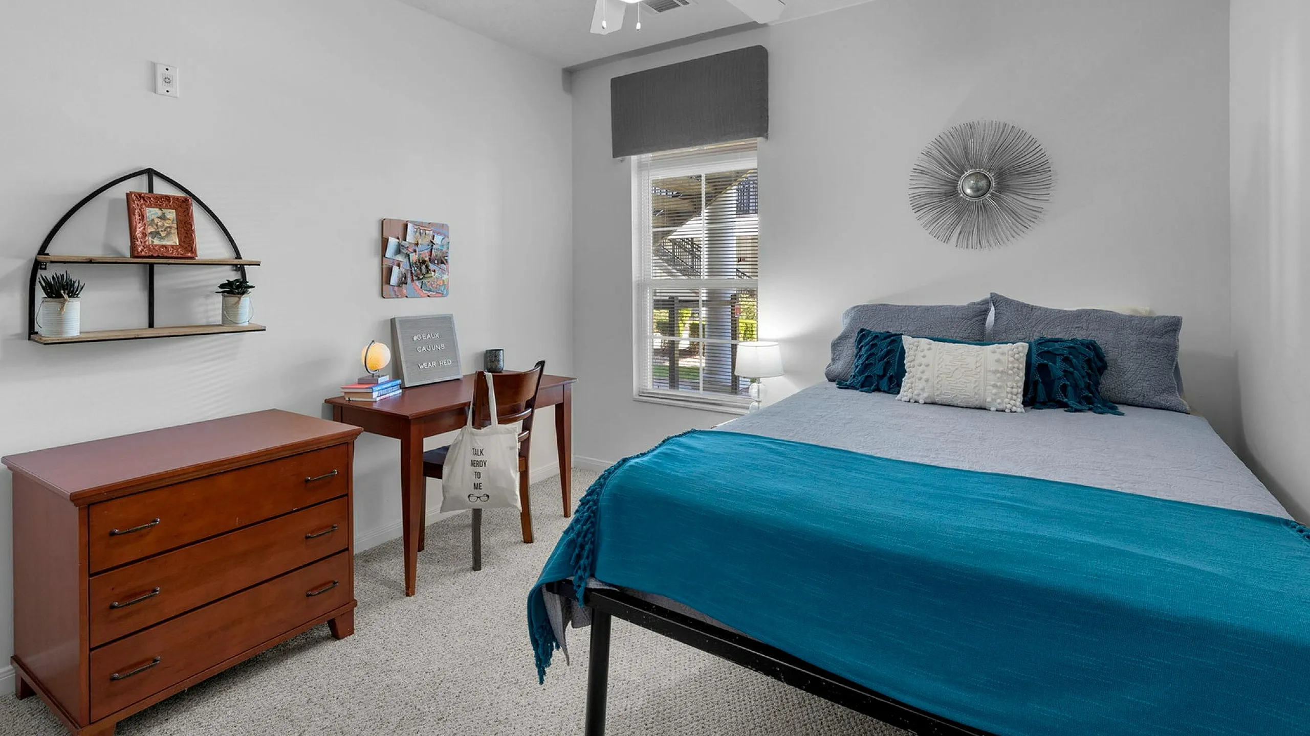 Inviting bedroom with cozy bed featuring vibrant blue accents, complemented by modern decor, workspace, and ample natural light.
