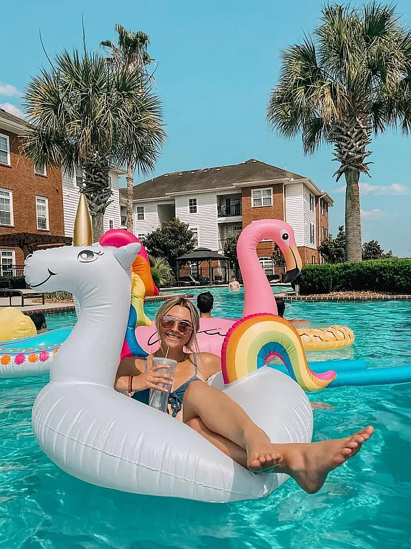 Vibrant poolside scene at a modern apartment complex featuring playful inflatable floats and palm trees, perfect for relaxation and summer fun.
