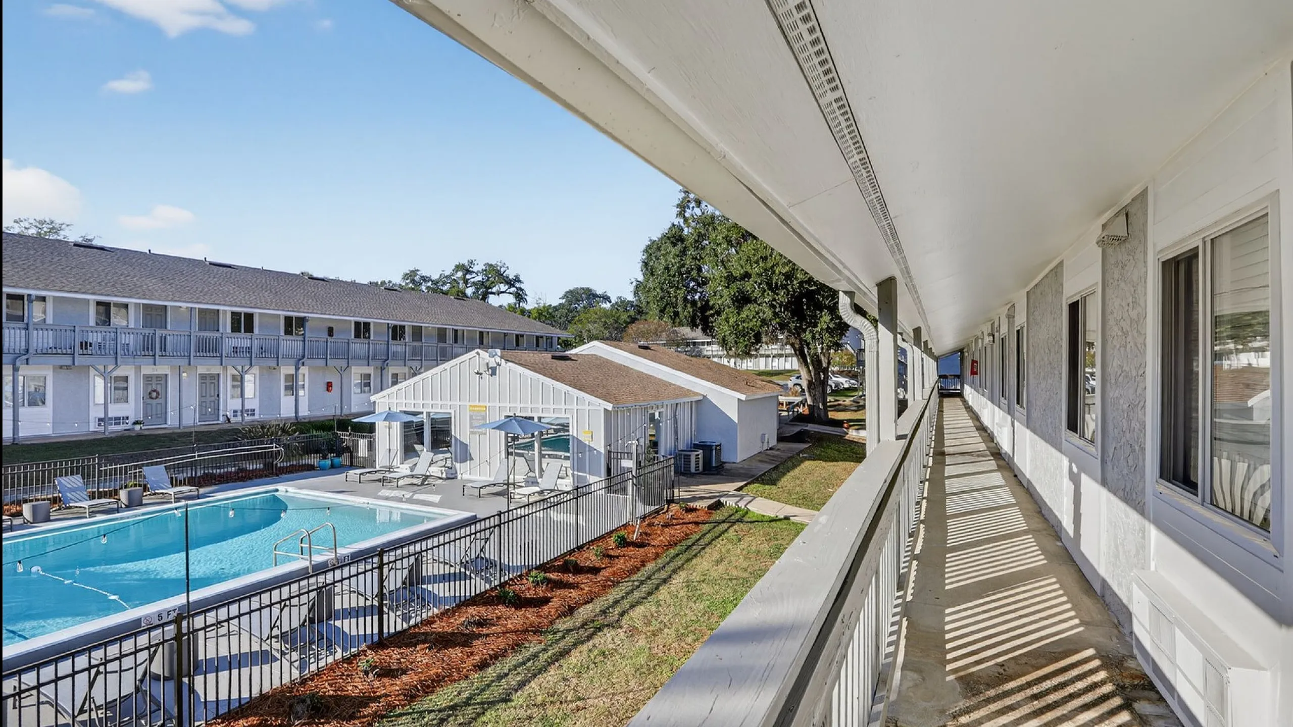 Inviting apartment complex with a sunny outdoor pool area and well-maintained walkway lined with windows, perfect for relaxation.