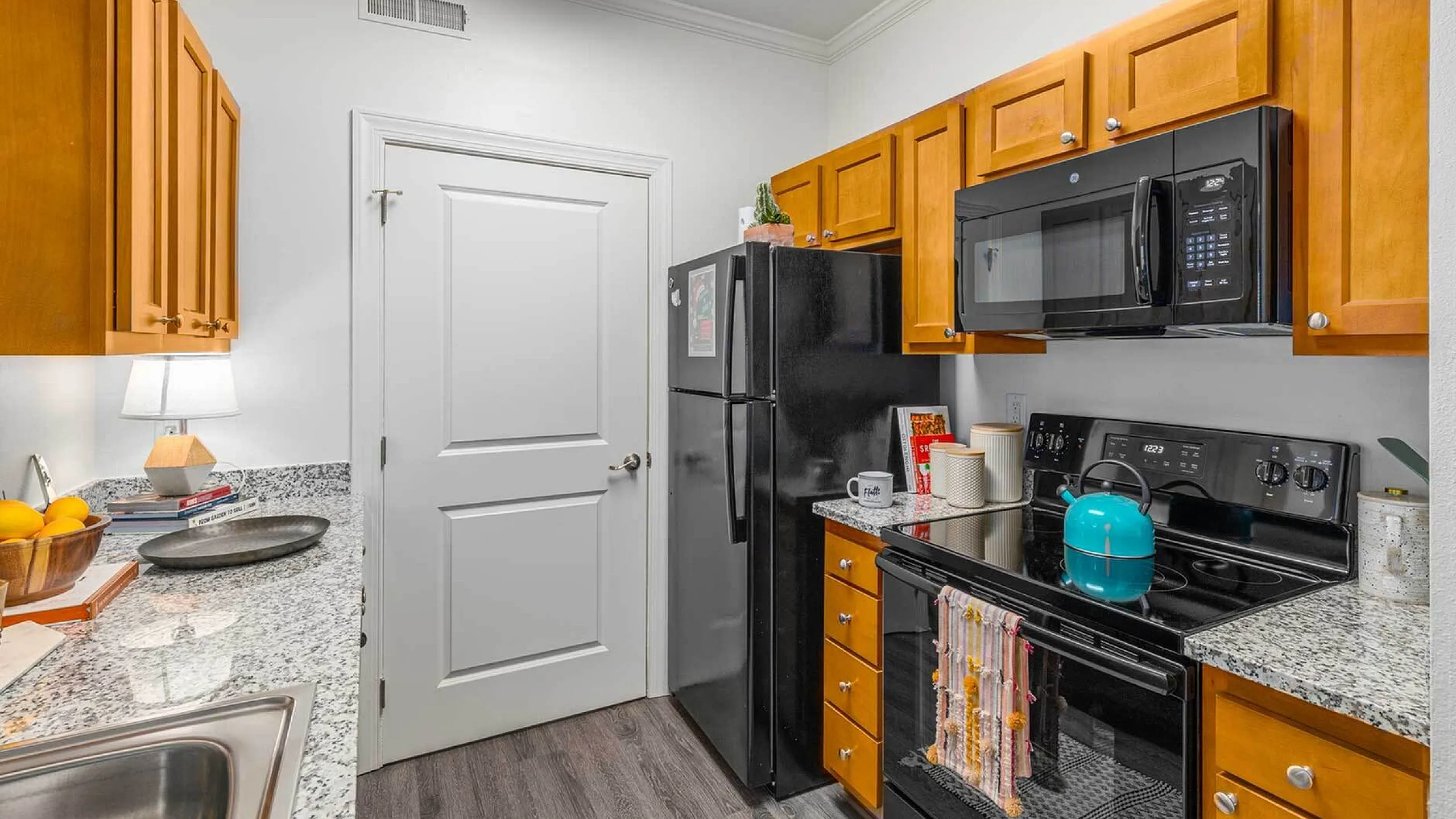 Modern kitchen featuring sleek granite countertops, warm wooden cabinets, and state-of-the-art black appliances, creating a stylish and functional cooking space.