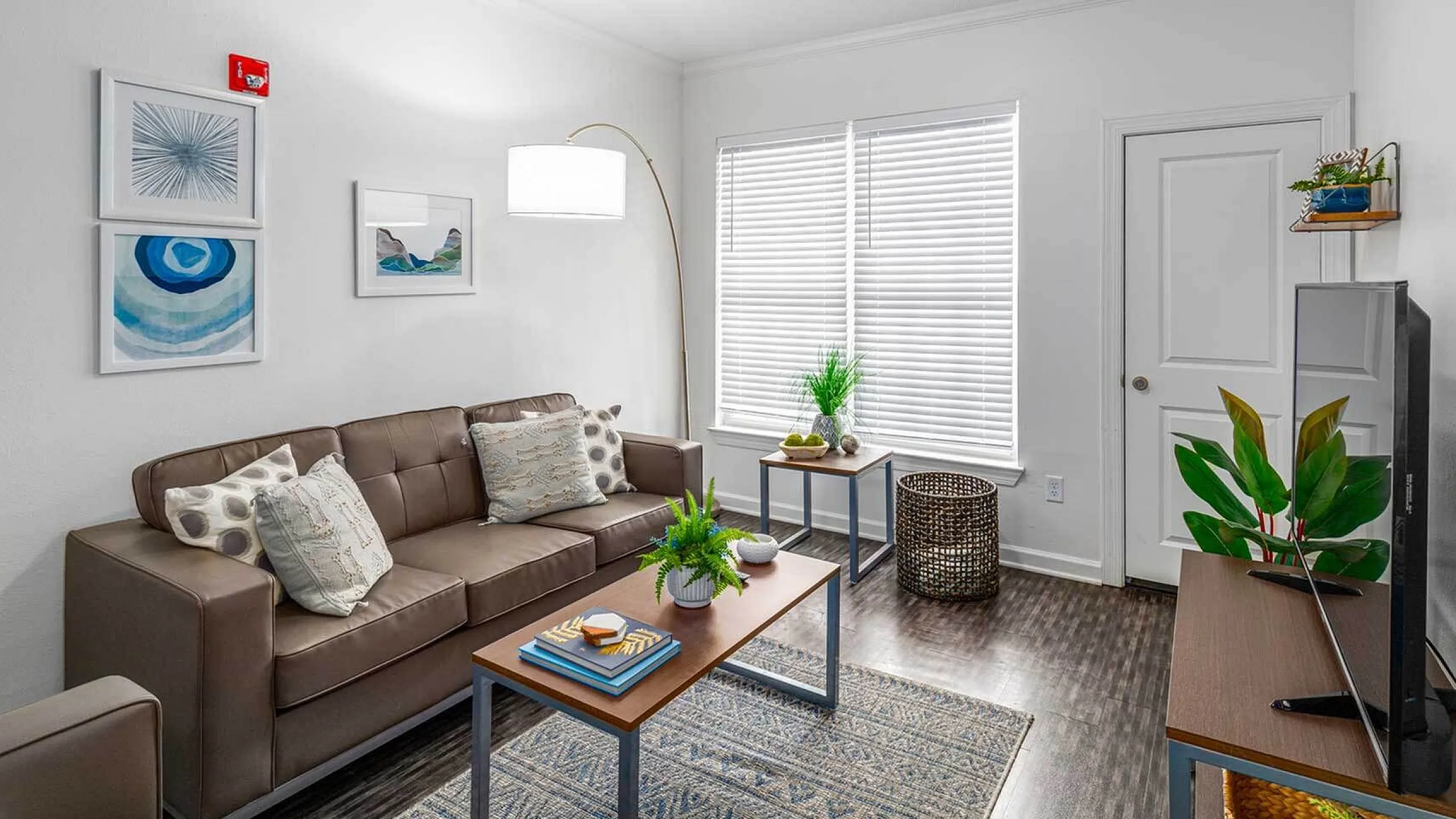Bright and inviting living room with modern decor, featuring cozy leather seating, stylish artwork, and lush greenery in a well-lit space.