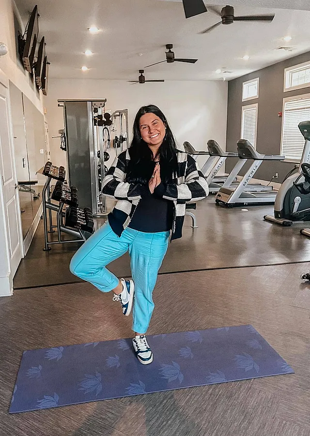 Bright and inviting fitness room with modern equipment, featuring a cheerful individual in a yoga pose on a mat, perfect for energizing workouts and relaxation.