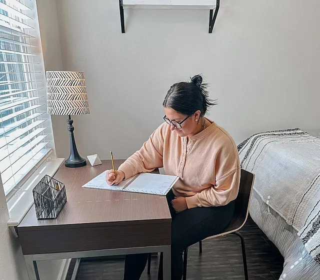 Bright and cozy apartment bedroom with a modern workspace, featuring a stylish desk, decorative lamp, and natural light streaming through the window.