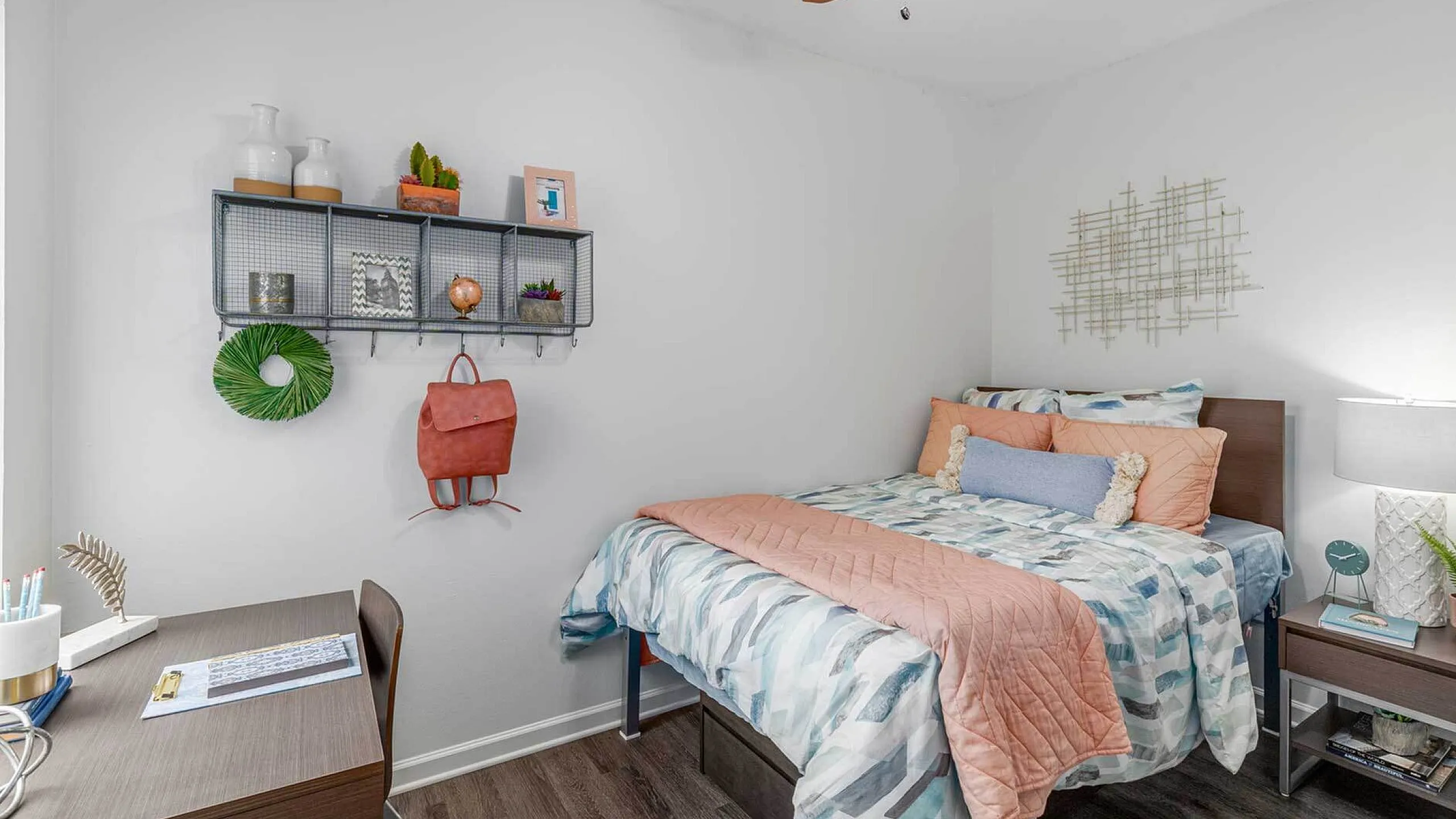 Cozy and stylish bedroom featuring a comfortable bed with pastel bedding, a sleek desk with modern decor, and chic wall shelving for personalized touches.