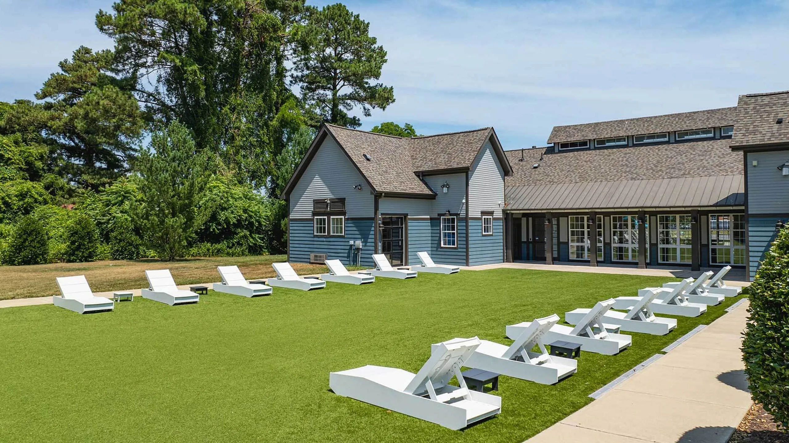 Charming outdoor area with modern lounge chairs and vibrant greenery, set against a stylish residential building under a clear blue sky.