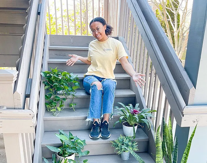 Cheerful person sitting on charming wooden stairs adorned with vibrant green plants in stylish pots, creating a serene and inviting outdoor ambiance.
