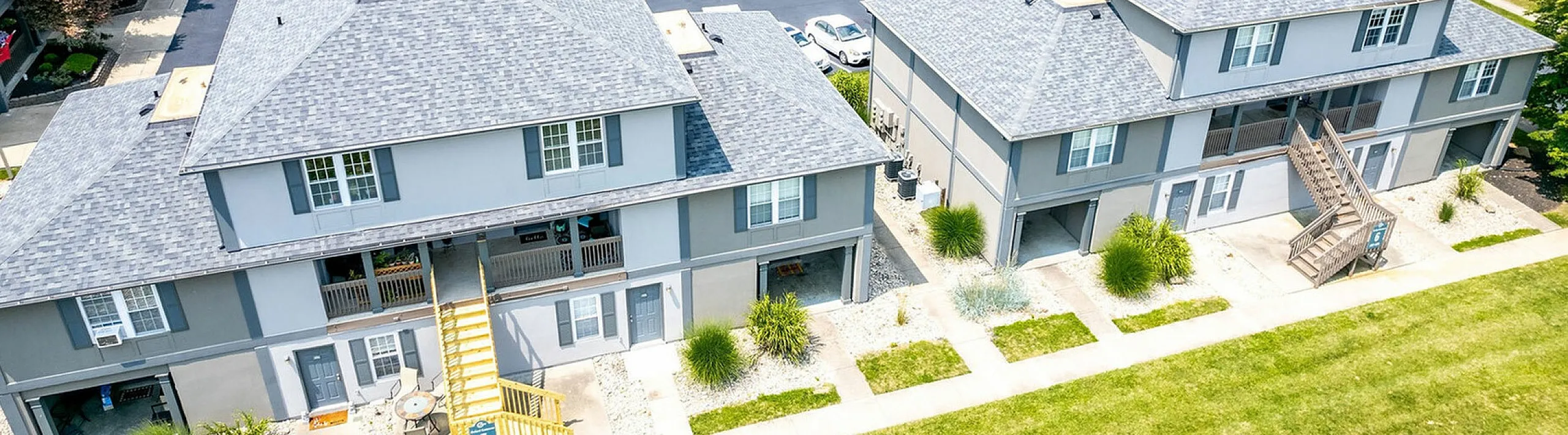 Aerial view of elegant apartment complex surrounded by lush greenery, showcasing spacious parking and well-maintained pathways.