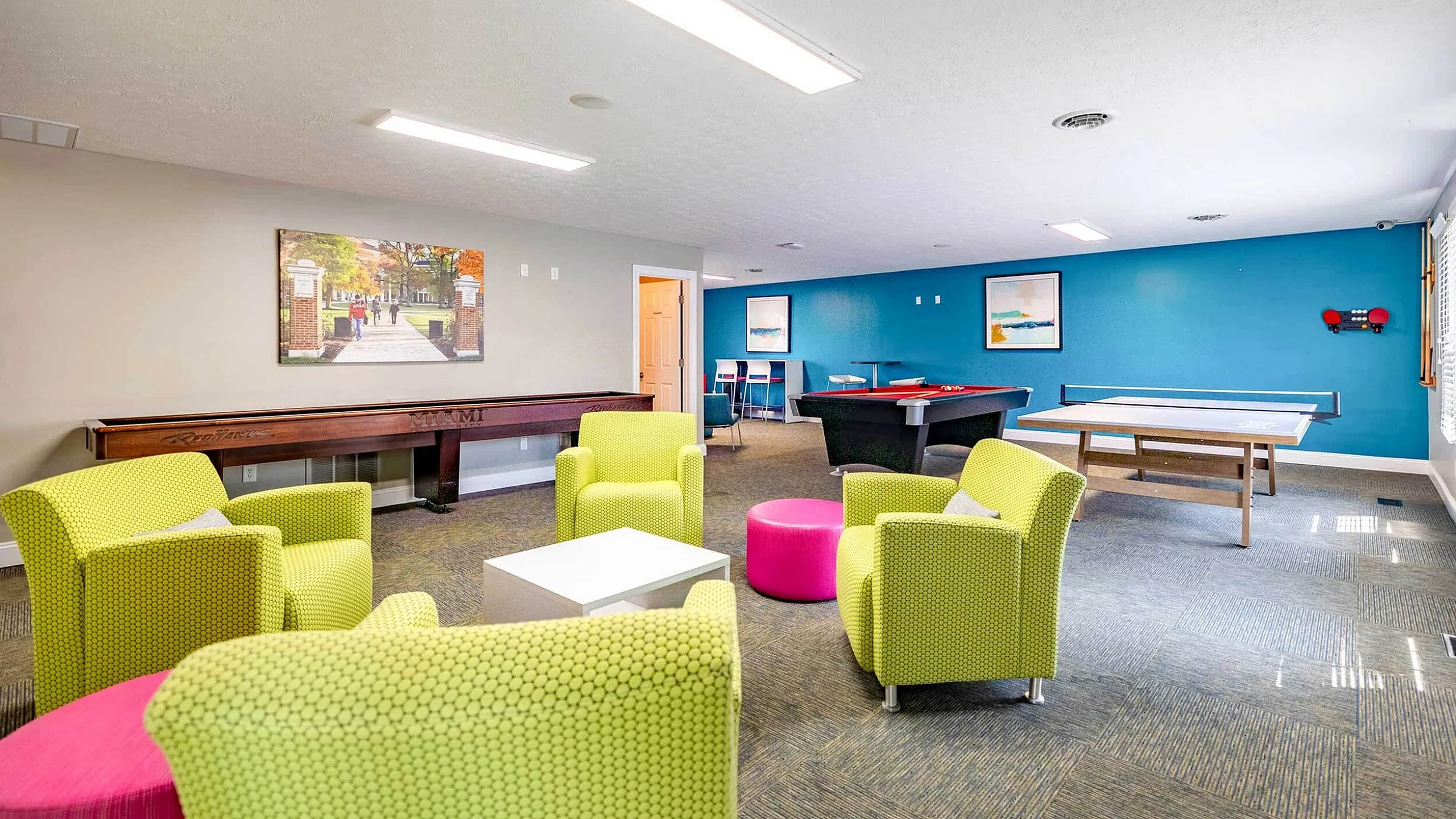 Bright and inviting recreation room with modern green chairs, a pool table, and a ping pong setup, perfect for relaxation and socializing.