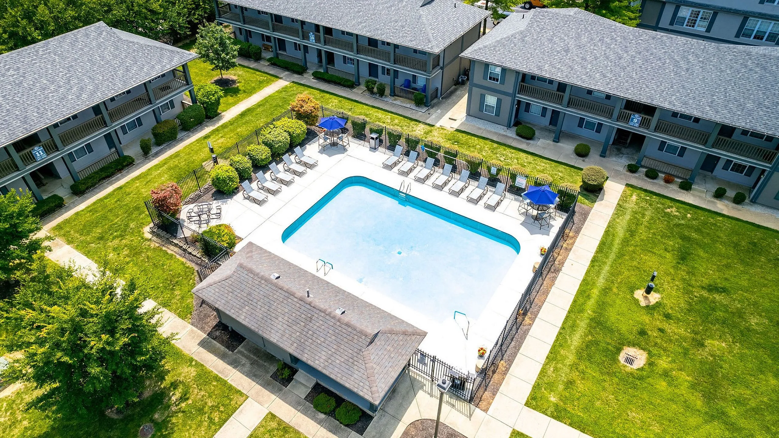 Aerial view of a charming residential complex with a pristine pool surrounded by sun loungers and vibrant greenery.