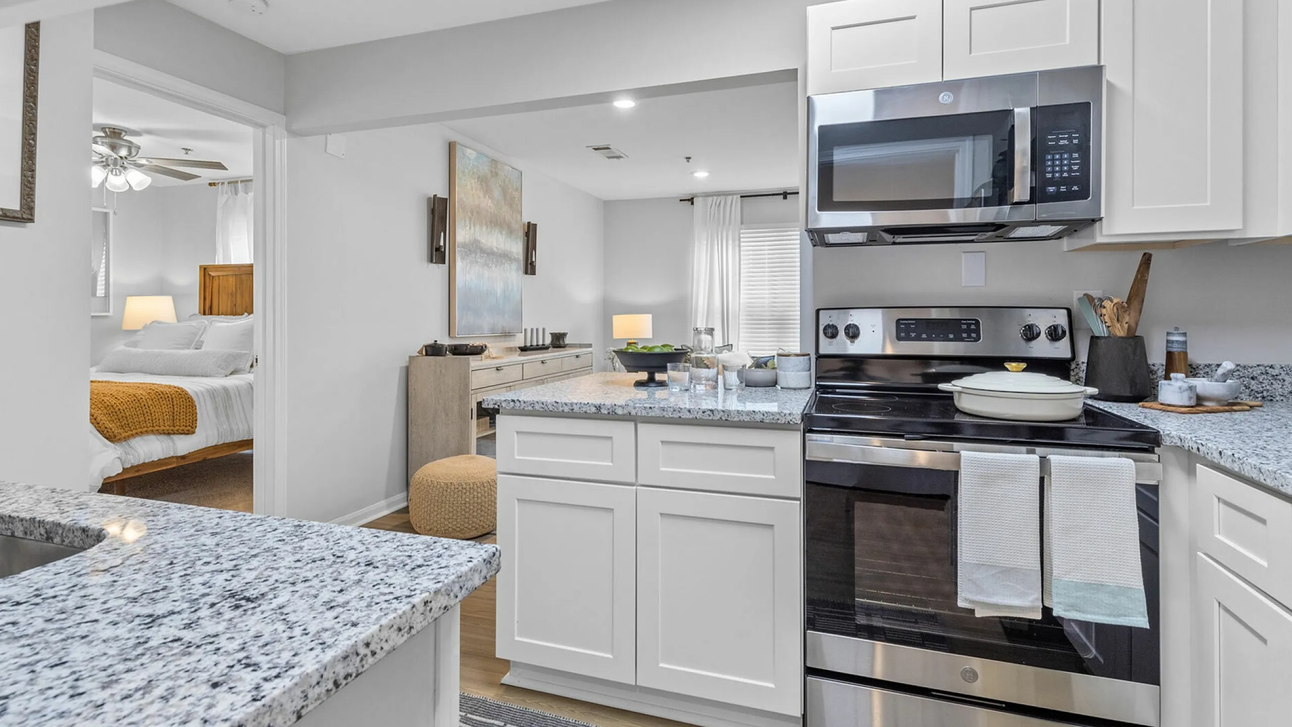 Modern kitchen with sleek granite countertops, stainless steel appliances, and open view into a cozy bedroom and stylish living area.