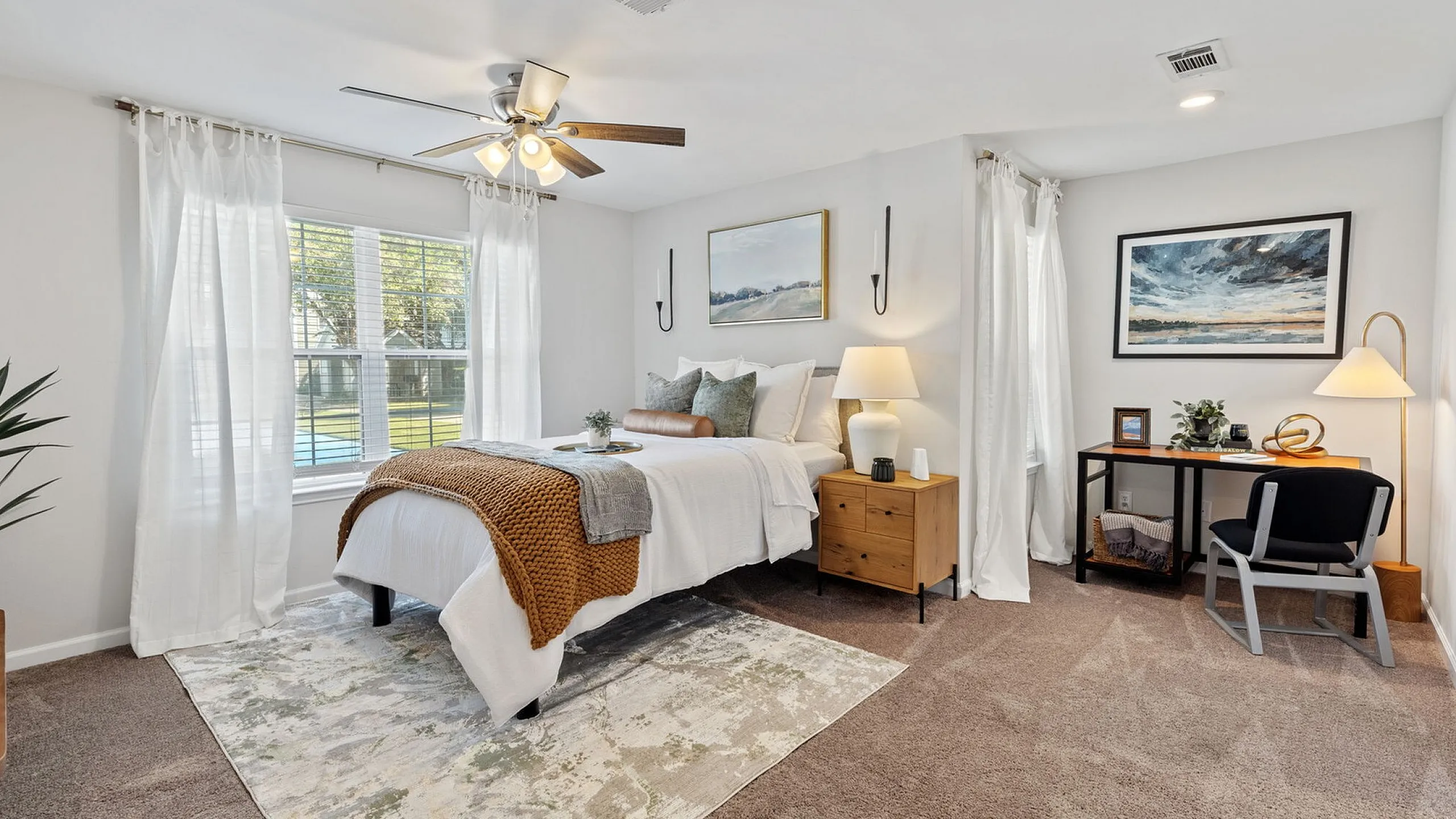 Charming bedroom filled with natural light, featuring cozy decor, a stylish workspace, and a lush view from large windows.