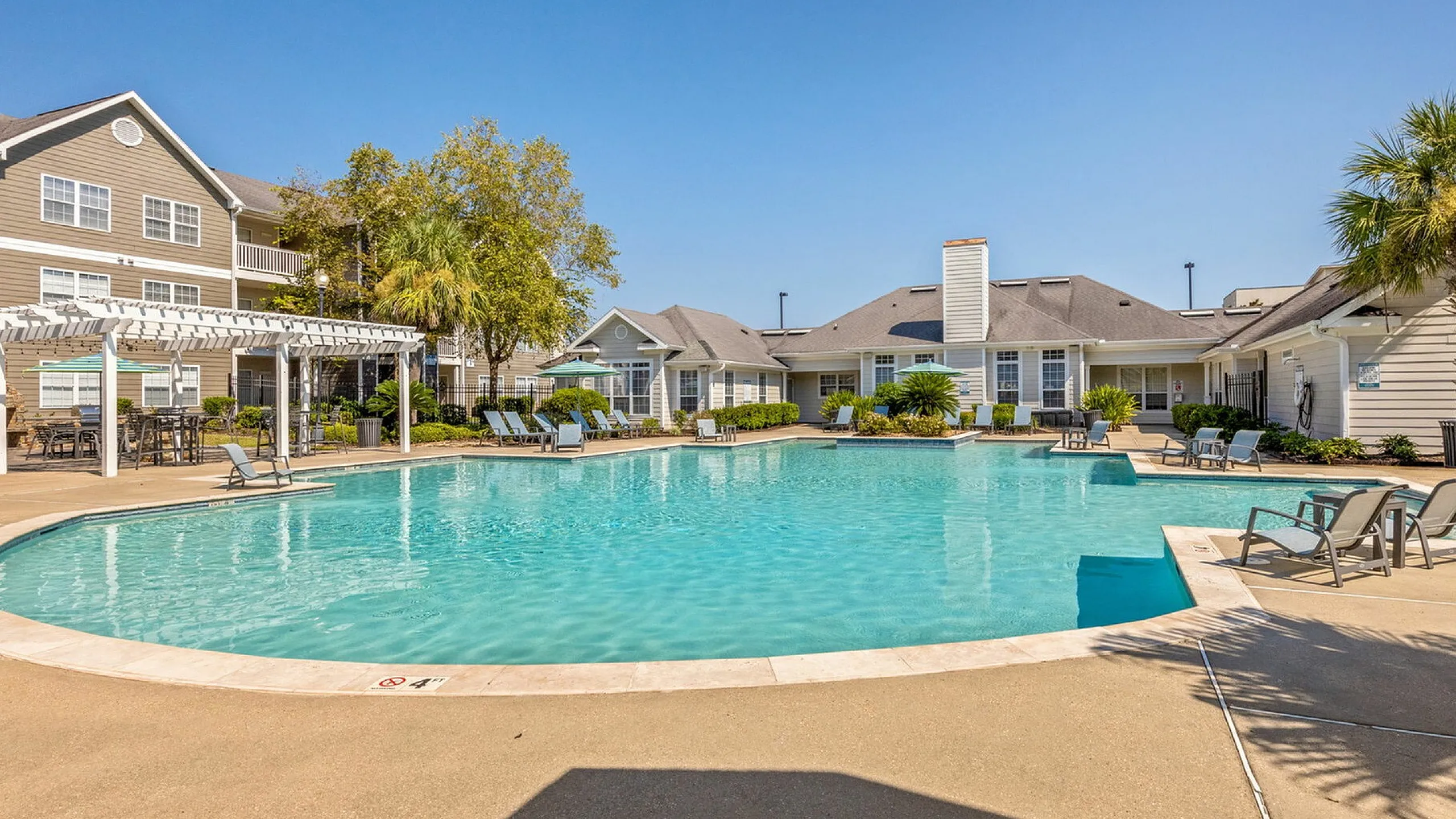 Luxurious apartment community with a sparkling outdoor pool, surrounded by lush greenery and elegant lounge chairs, perfect for relaxation.