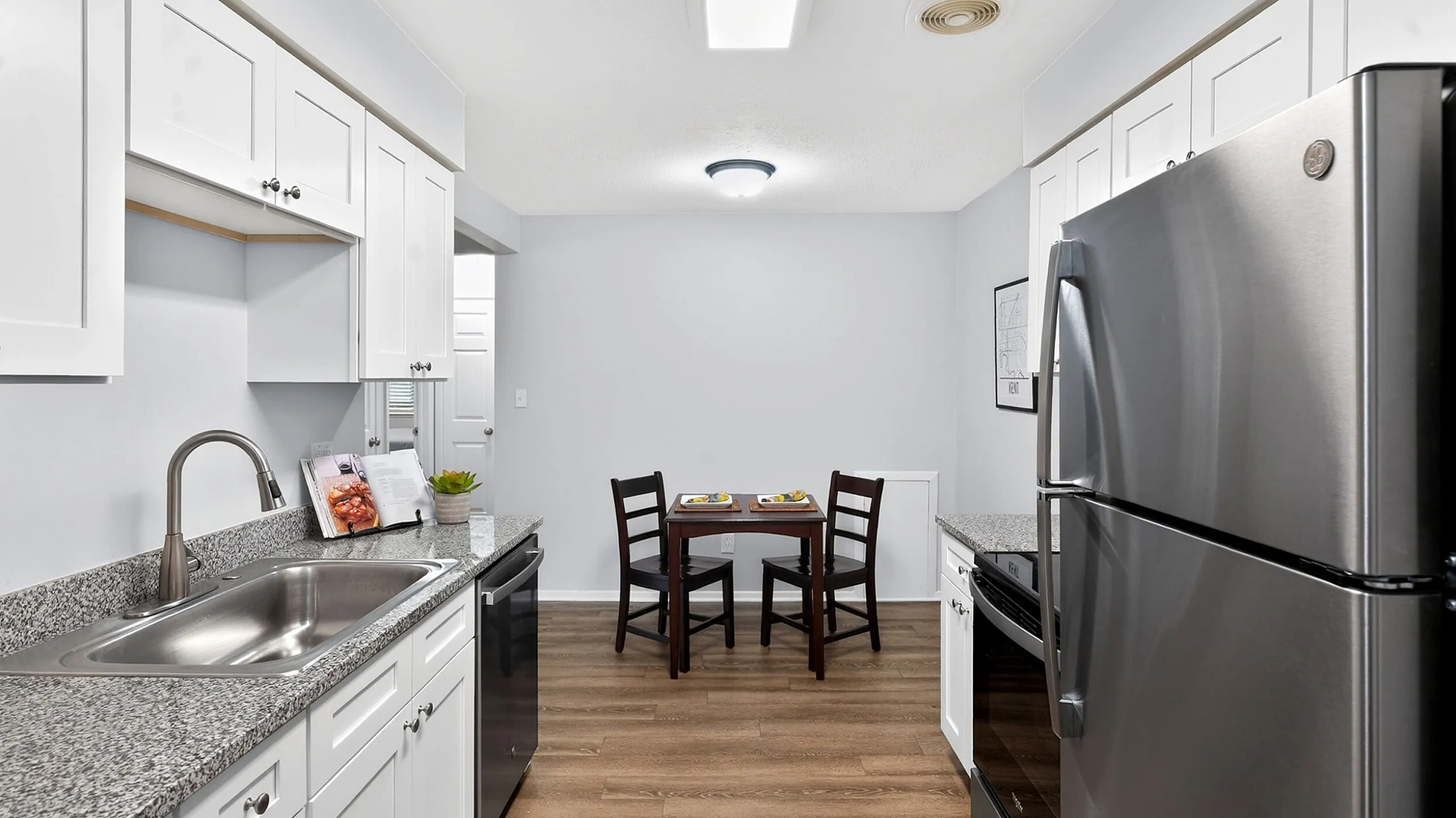 Contemporary kitchen with sleek stainless steel appliances, granite countertops, and elegant white cabinetry, leading to a cozy dining area with a stylish wooden table and chairs.