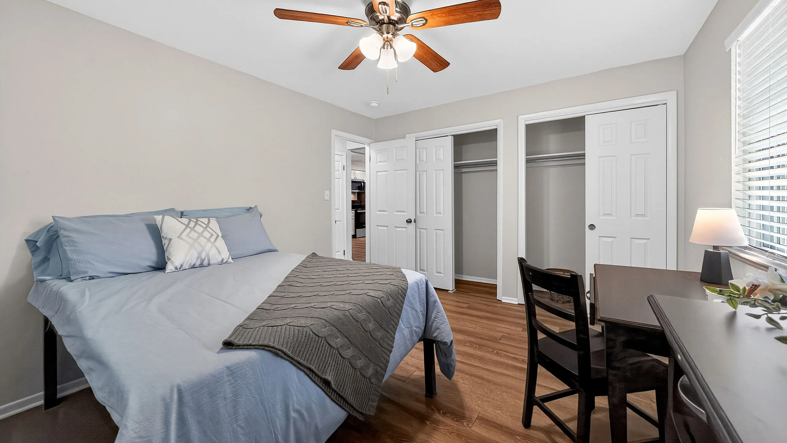 Inviting bedroom with elegant wood flooring, stylish ceiling fan, and cozy workspace, offering ample storage with double closets.