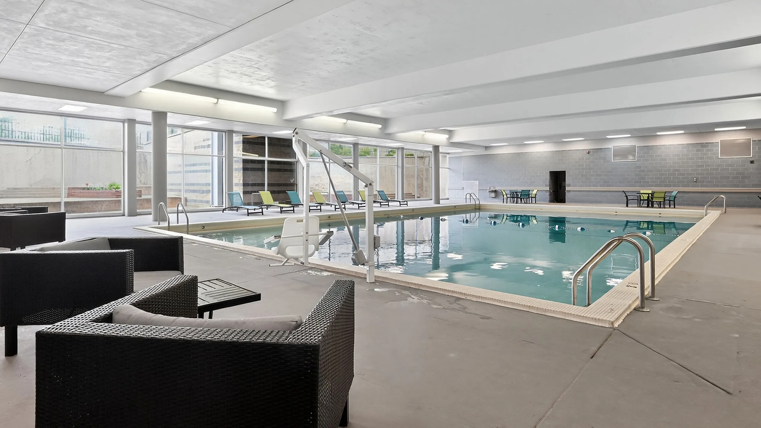 Spacious indoor pool area with modern lounge seating and bright natural lighting, perfect for relaxation and leisure.