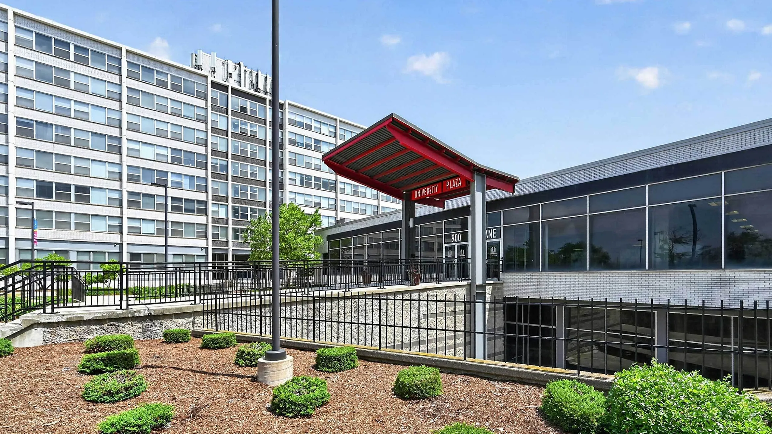 Modern apartment exterior with landscaped garden entrance, featuring sleek architecture and large windows at University Plaza.