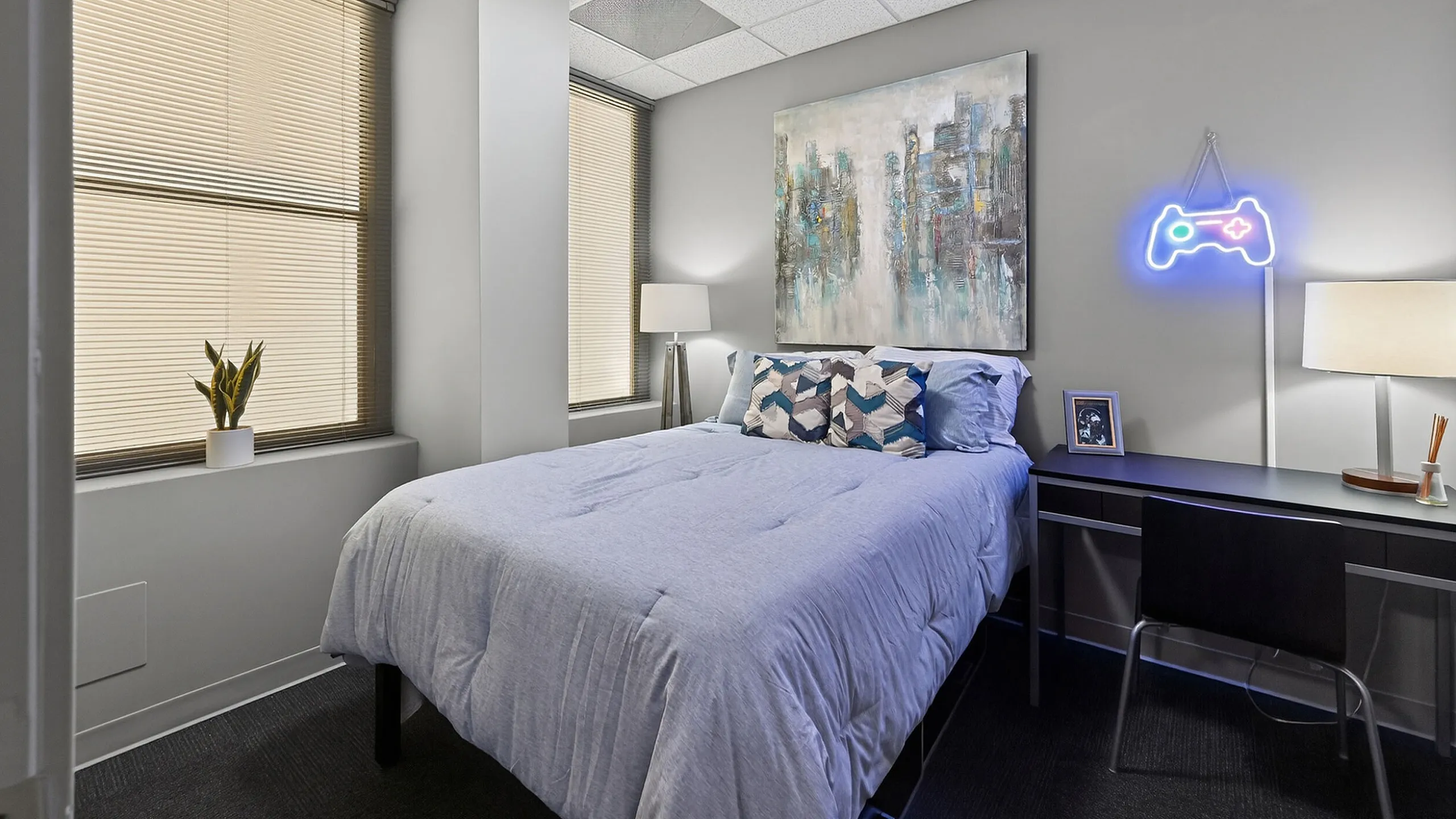 Modern bedroom with cozy bed, stylish artwork, neon game controller decor, and ample natural light from large windows.