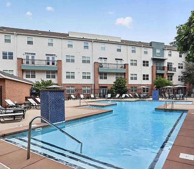 Inviting apartment complex with a sparkling outdoor pool, surrounded by stylish lounge chairs and lush greenery.