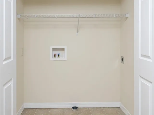 Interior of a laundry closet at Embassy Apartments in Ozark, Missouri, showing a recessed alcove with stacked washer/dryer hookups, utility connections, and an upper shelf against a neutral wall.