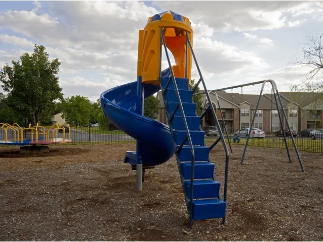 Outdoor playground at Willow Creek Apartments featuring a blue spiral slide and swing set, offering fun for families and children.
