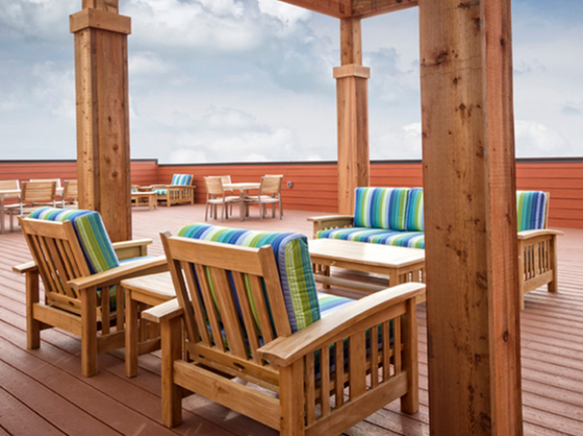 Cozy rooftop seating area under a wooden pergola with cushioned wooden chairs and a coffee table, surrounded by additional tables and chairs.