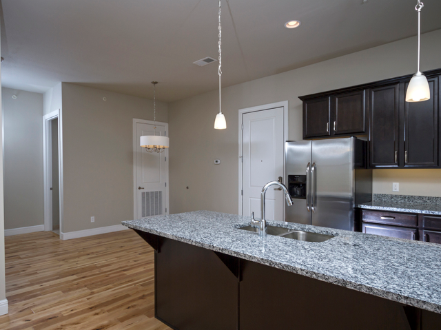 Close-up of a granite kitchen island with a sink and pendant lighting, facing the open layout of the apartment.