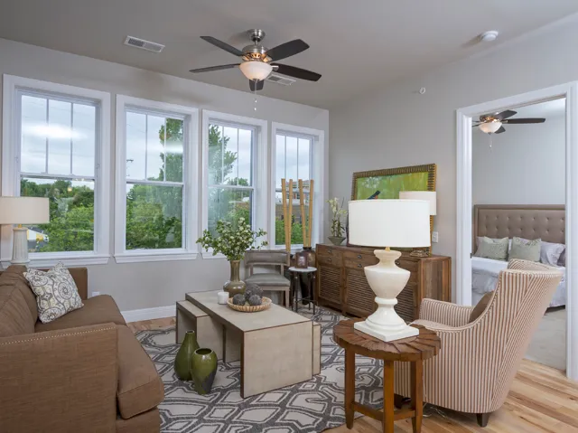 Bright and stylish living room with large windows, a ceiling fan, modern furniture, and a patterned rug, adjacent to a bedroom.