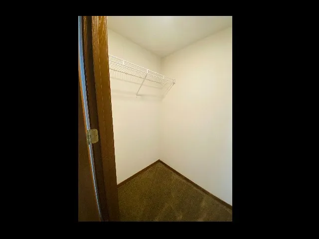 Empty walk-in closet with white walls, brown trim, and two wire shelves, offering ample storage space inside a Huntley Ridge East apartment.