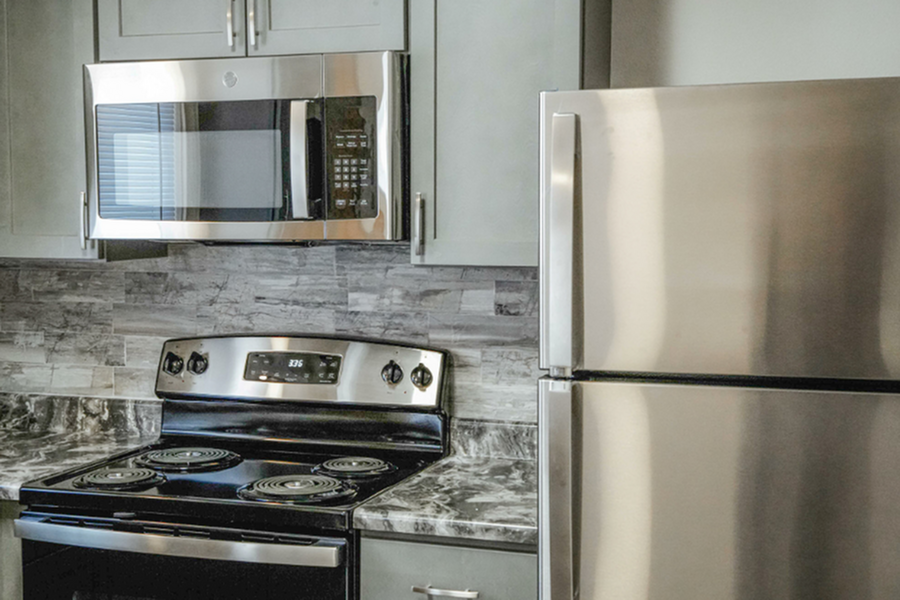 Modern kitchen featuring sleek stainless steel appliances, including a microwave, stove, and refrigerator, set against a chic grey backsplash.