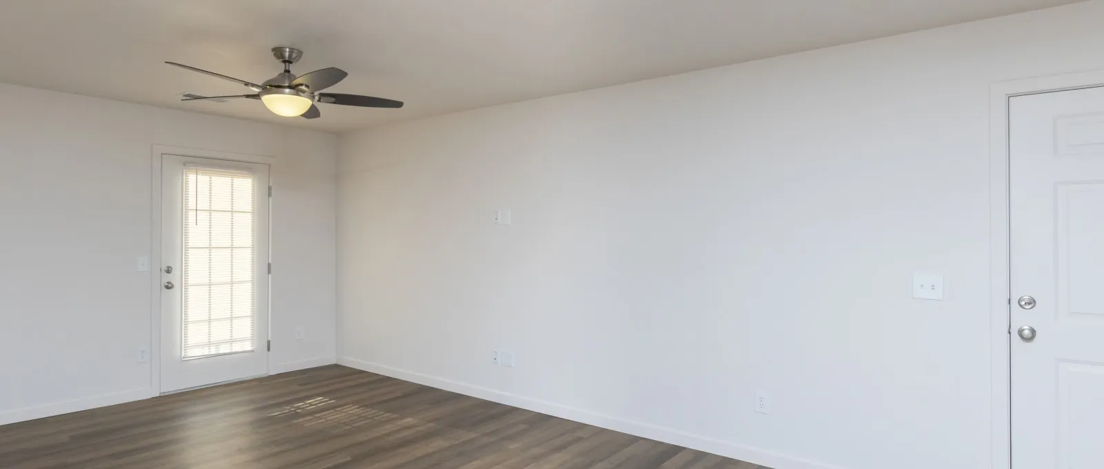 Empty living room with white walls, ceiling fan, and wood-style flooring at Republic Palms Apartments, ready for personal decor and furnishings.