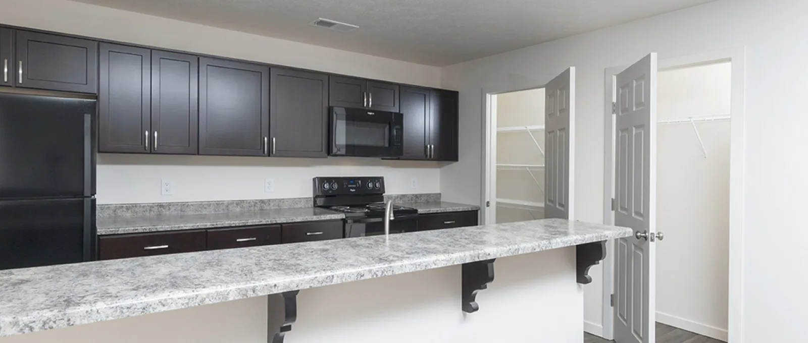 Modern kitchen at Republic Palms Apartments with dark cabinetry, black appliances, and a speckled granite-style countertop with bar seating.