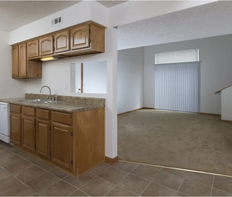 Open-concept kitchen with wood cabinetry and granite-look countertops, connected to a carpeted living space with sliding patio doors.